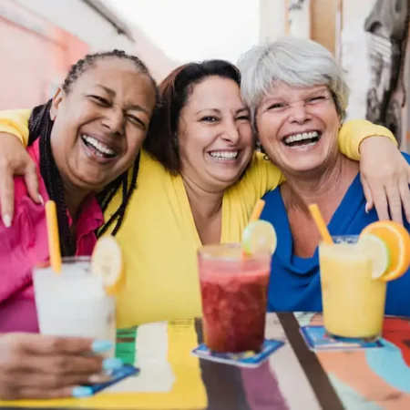 A group of three women laughing together with drinks in front of each of them