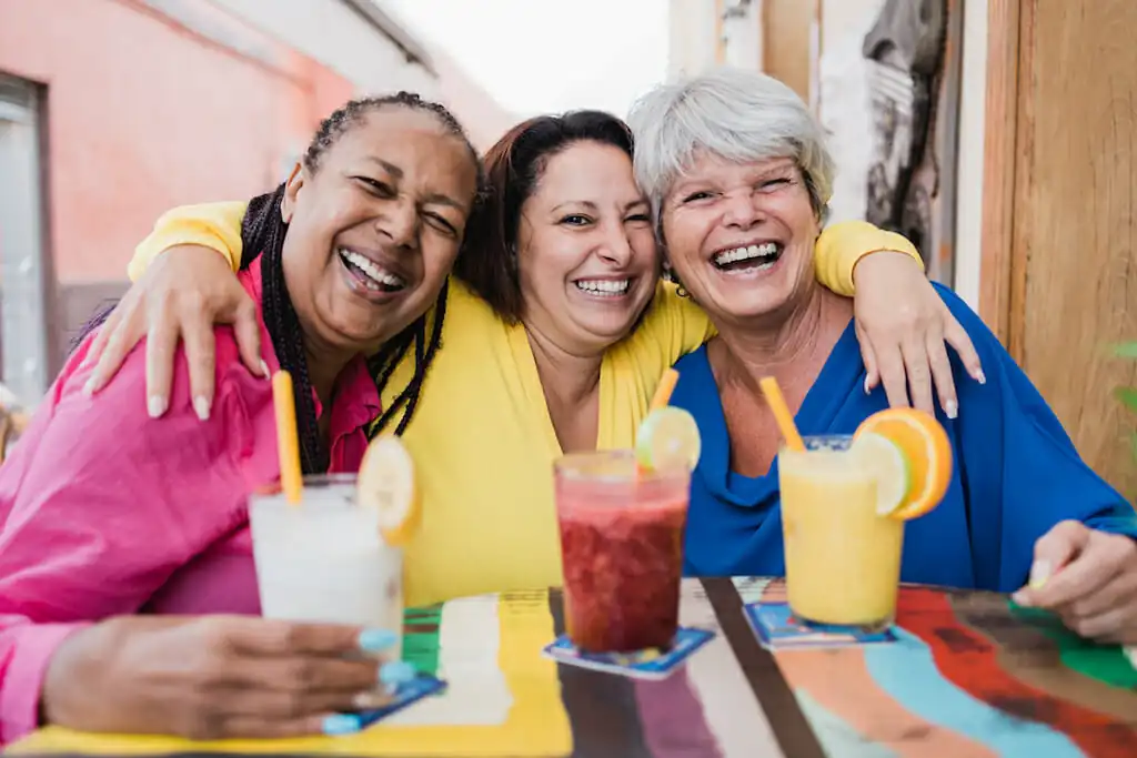 A group of three women laughing together with drinks in front of each of them