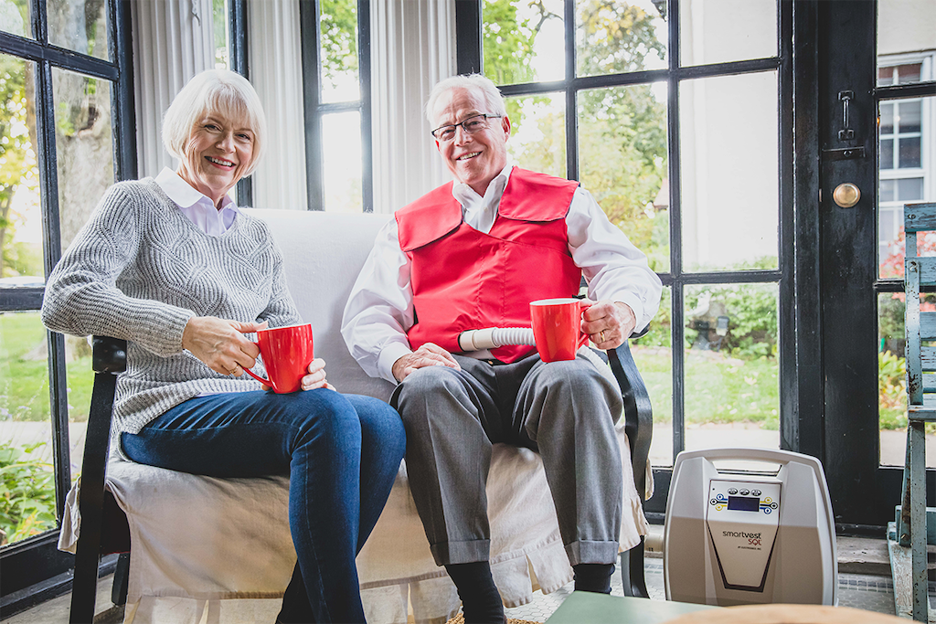 An older couple sits on their sofa while drinking coffee together