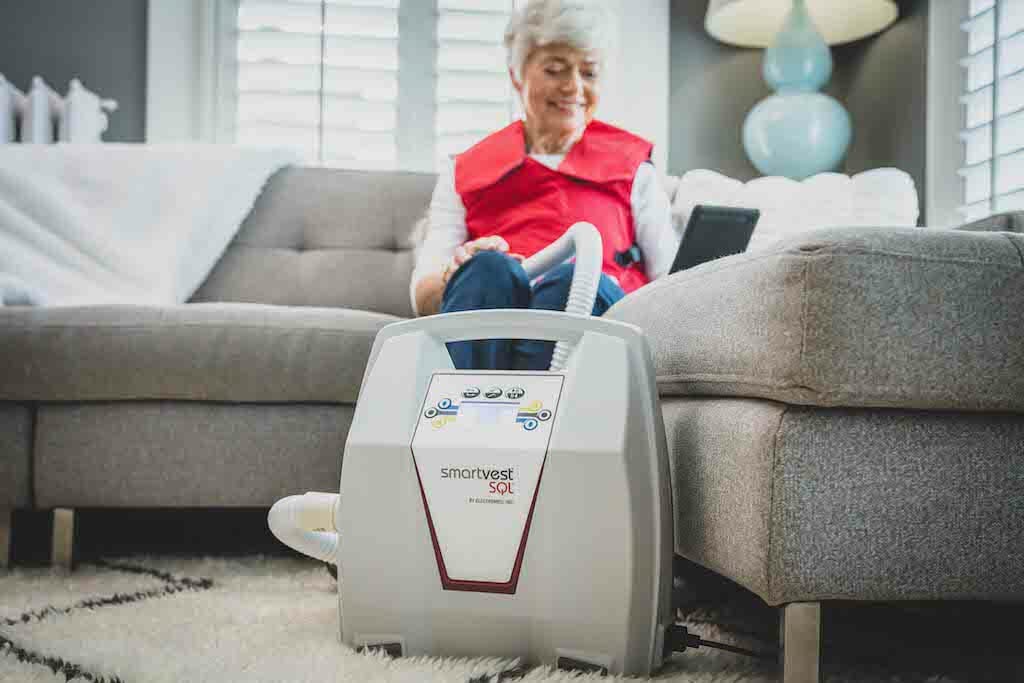 Woman sitting on couch at home using HFCWO vest therapy.