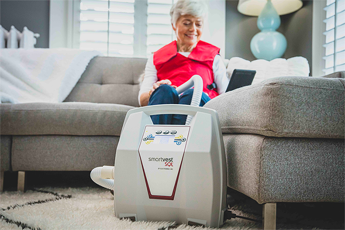 Older woman using SmartVest Airway Clearance System while browsing on tablet.