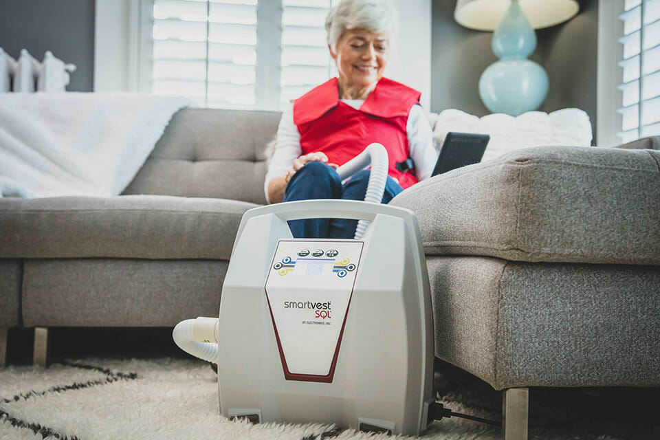 Woman on couch using her SmartVest Airway Clearance System
