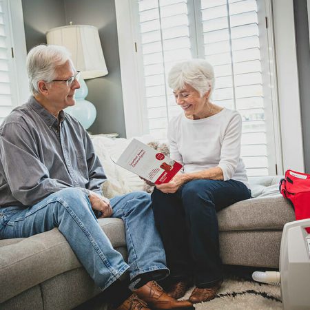 An older couple sits on a couch while the wife looks through a SmartVest brochure