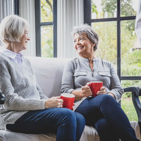 Two women smiling while having coffee on a couch together