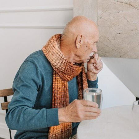 A man coughs while holding a glass of water