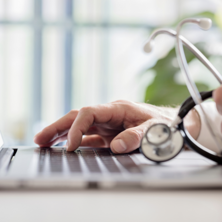 A doctor holds their stethoscope while working on a laptop