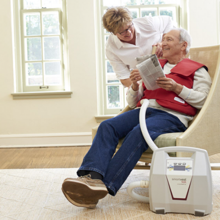 A woman greets a man from behind his chair as he does his SmartVest therapy