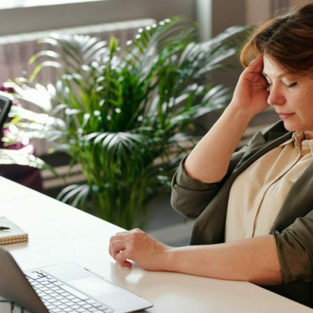 A woman holds her head while closing her eyes at her desk