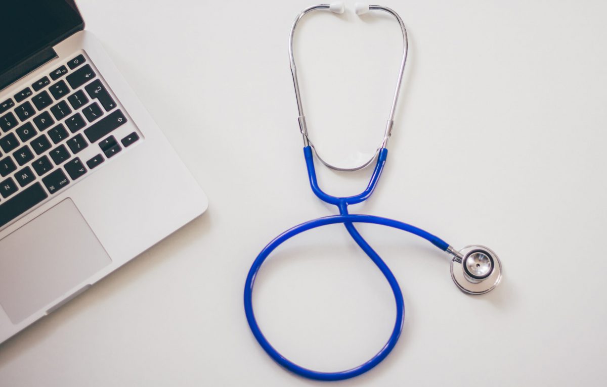 A stethoscope rests on a table near a laptop