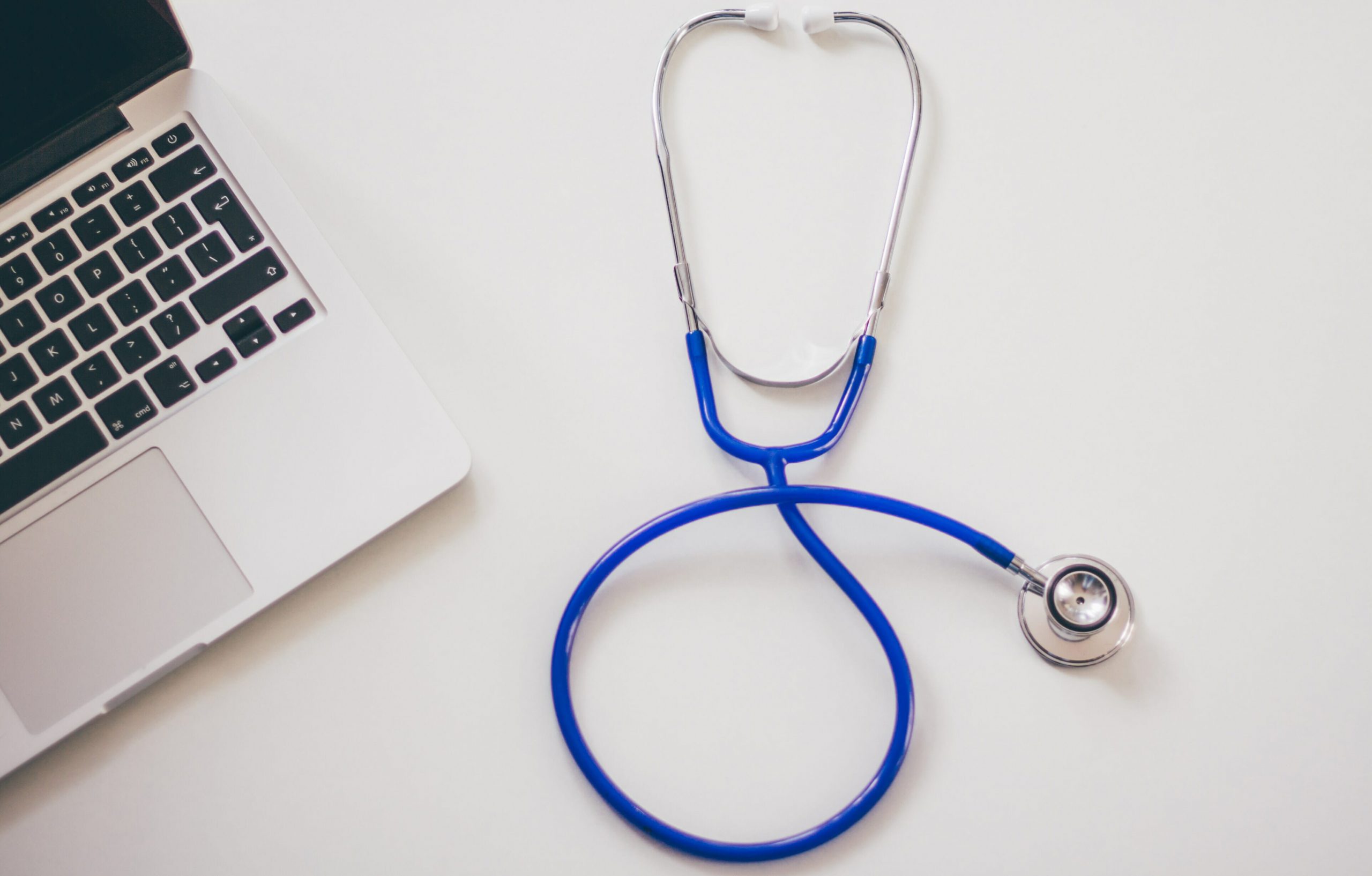 A stethoscope rests on a table near a laptop