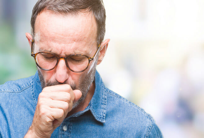 Man living with COPD coughing into hand.