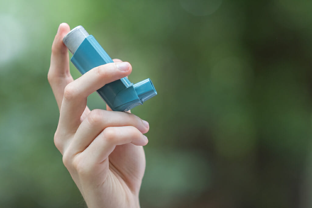 Woman outside holding inhaler to help relive asthma symptoms.