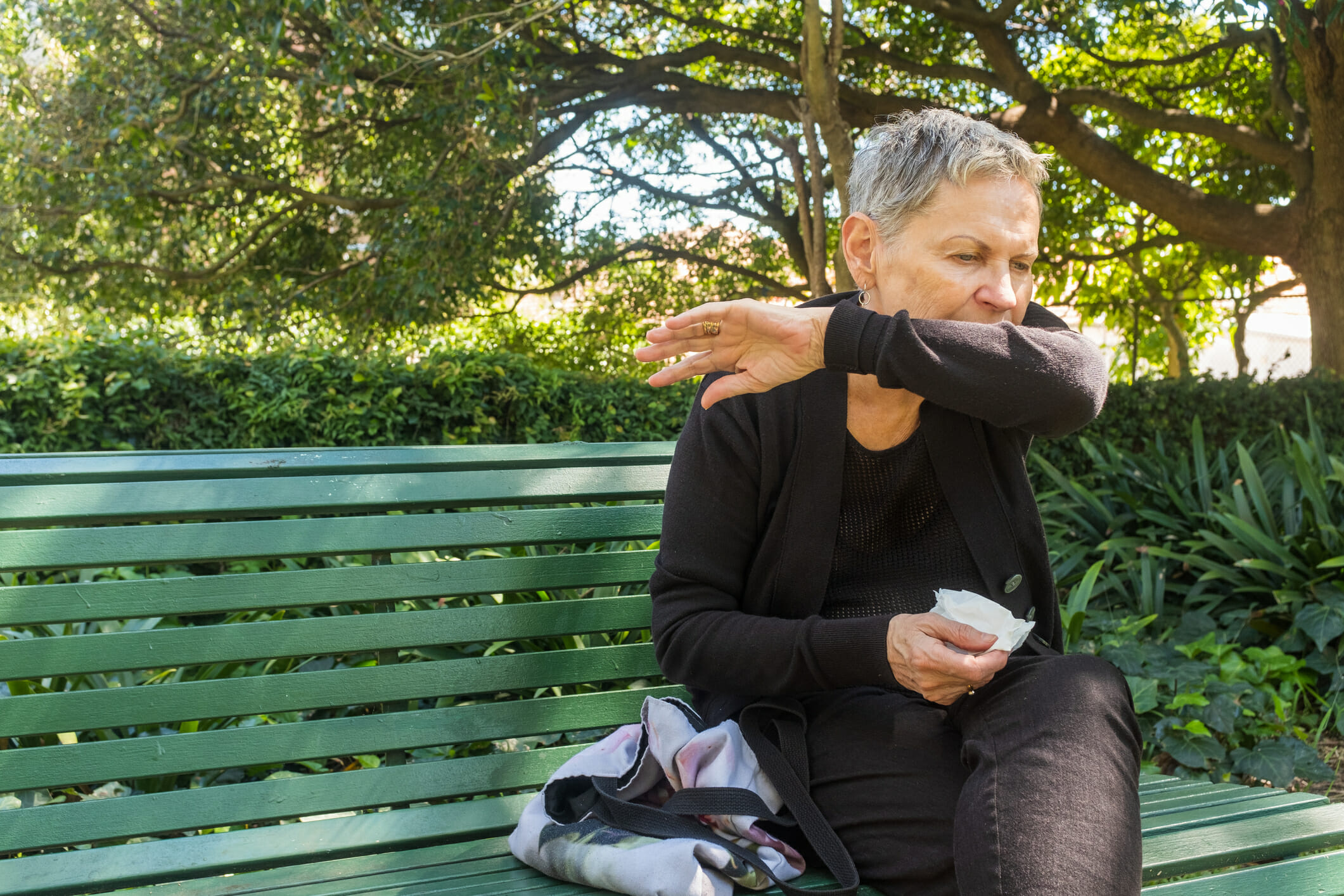 A woman coughs into her elbow while outdoors