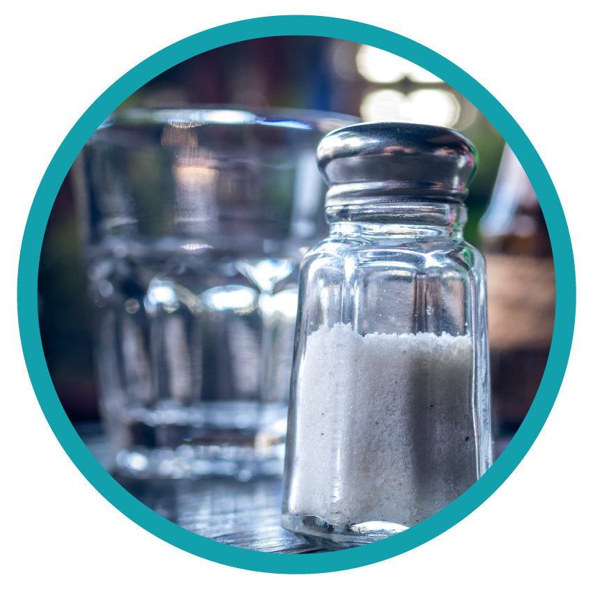 Salt Shaker in front of water glass on table.