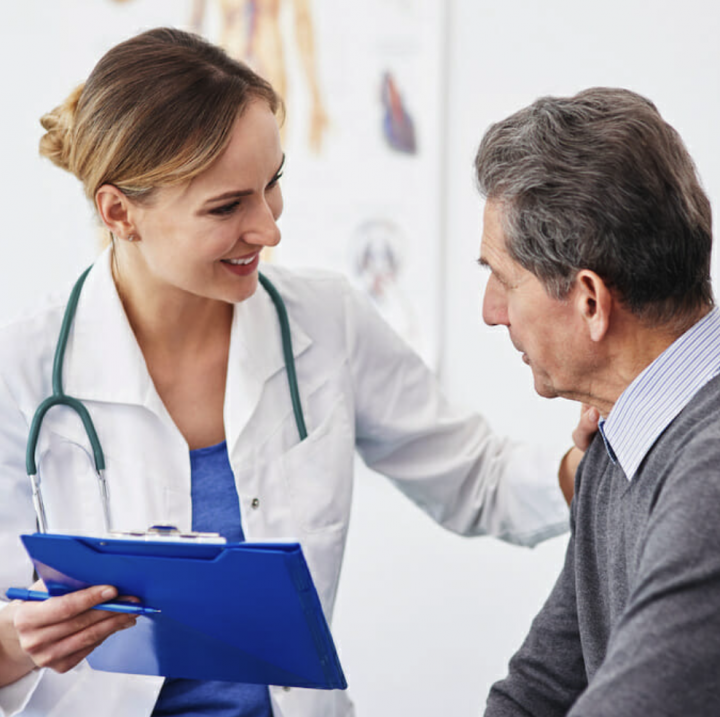 A female doctor holds her patient's shoulder in one hand and a clipboard in the other