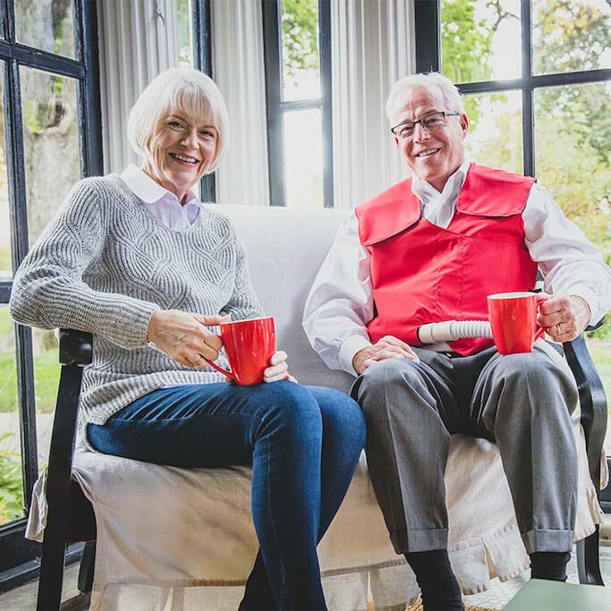 A couple drinks coffee together in a porch room while the husband uses his SmartVest
