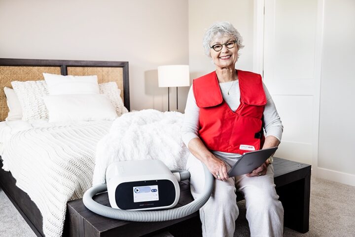 SmartVest user sitting on bed while using airway clearance device.