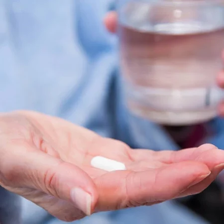 DPP1 medications in the palm of a hand with a glass of water in the background.