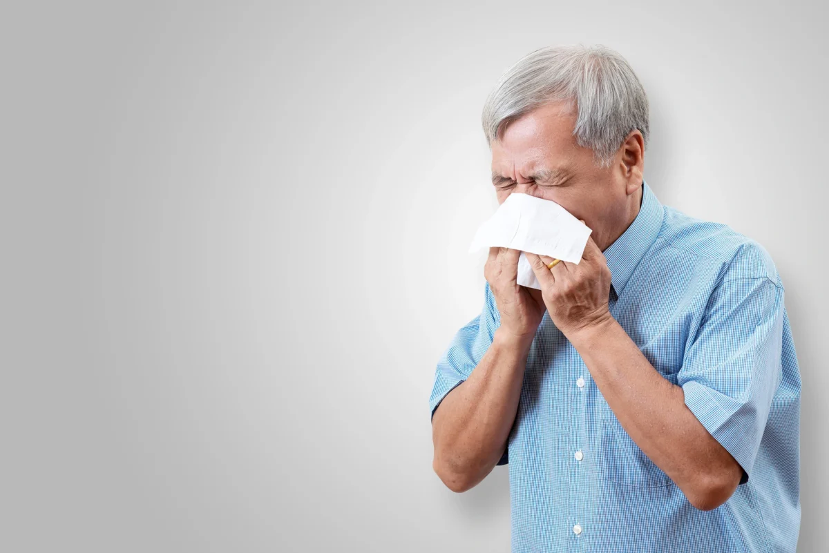 Elderly man sneezing into a tissue.