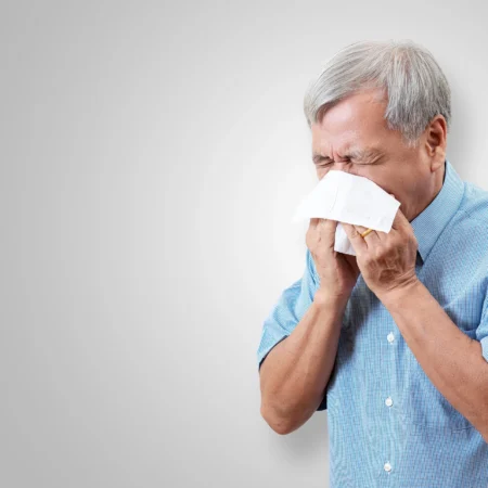 Elderly man sneezing into a tissue.