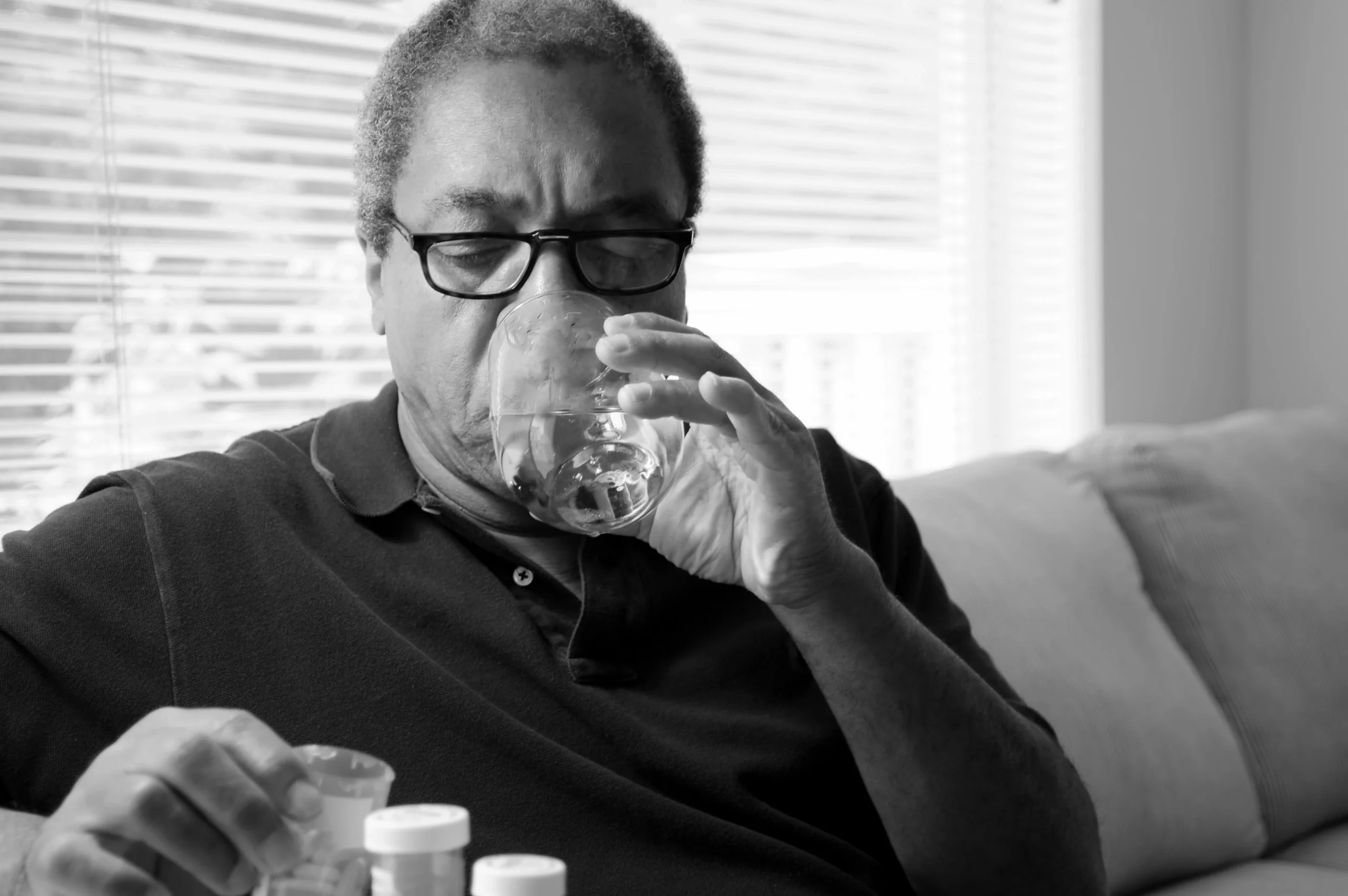 Black and white photo of Black man taking medication for bronchiectasis with a glass of water.
